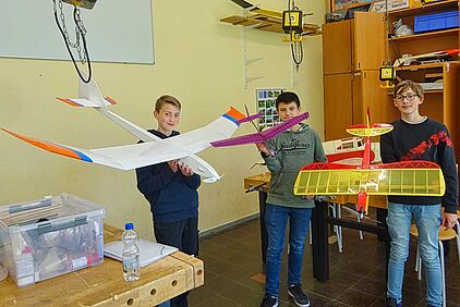 Drei Jugendliche zeigen restaurierte Modellflugzeuge